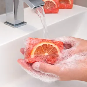Handmade grapefruit soap bar in use with rich foam under running water in bathroom sink