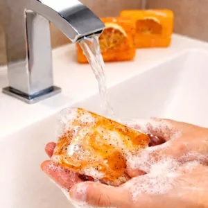 Handmade orange soap being washed with foam under running water